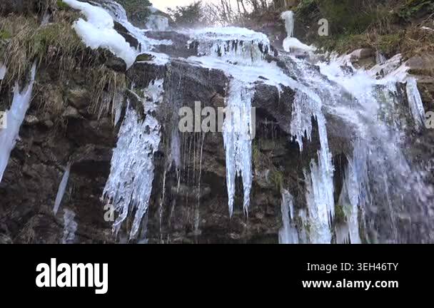 White icicles hang from frozen waterfall as water pours over rocky ...