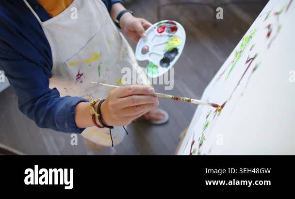 Senior Asian male painter dipping brush into palette, refining marks on ...