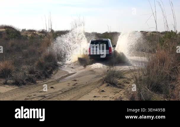 Aerial view of 4x4 suv splashing muddy water while crossing flat ...