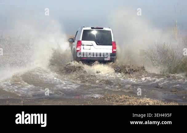 Aerial view of 4x4 suv splashing muddy water while crossing flat ...