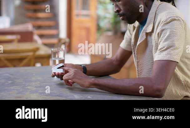 African American man sitting at worn table, spotting white device and ...