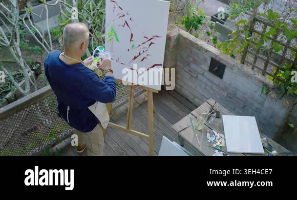 Senior Asian man dipping brush into palette, painting green tree ...