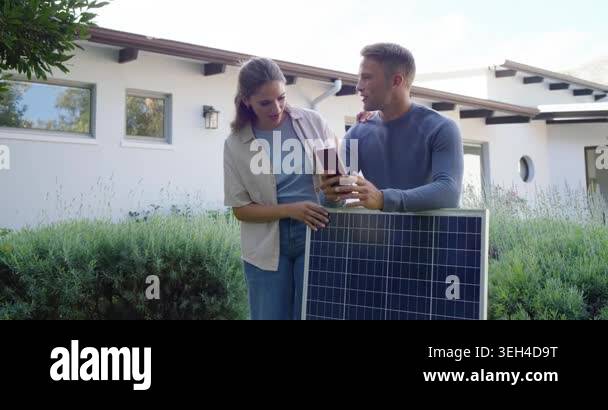 Diverse couple at modern house holding solar panel pointing to roof and ...