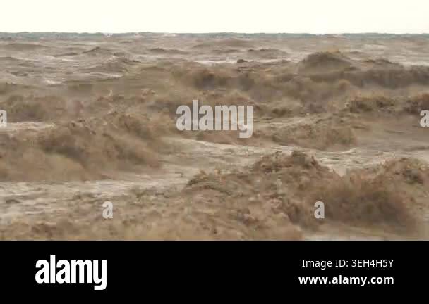 Brown muddy waves churn at river mouth where floodwaters meet the sea ...