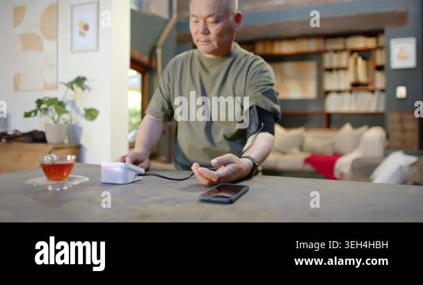 Senior Asian Chinese man pressing monitor with cuff on left arm ...