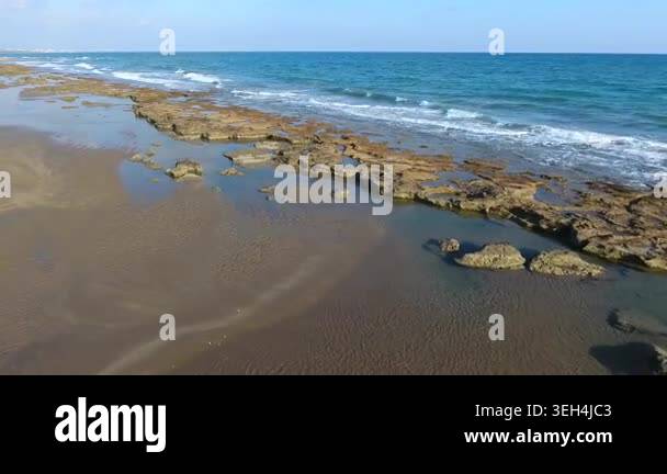 Aerial rocky reef barrier lines the shore as waves wash across an empty ...