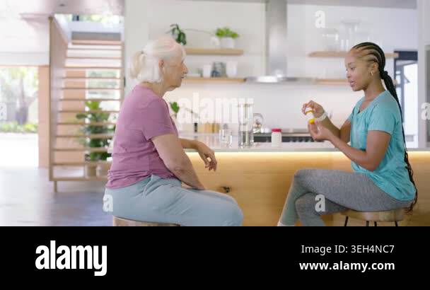 African American carer showing pill bottle, pointing, helping senior ...