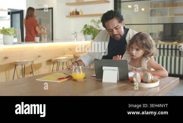 African American dad leaning in guiding school-age daughter at table ...