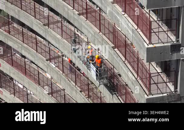 Construction workers hang in a suspended basket while repairing a tall ...