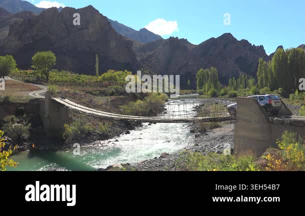 A car crosses a dangerous wooden suspension bridge supported by steel ...