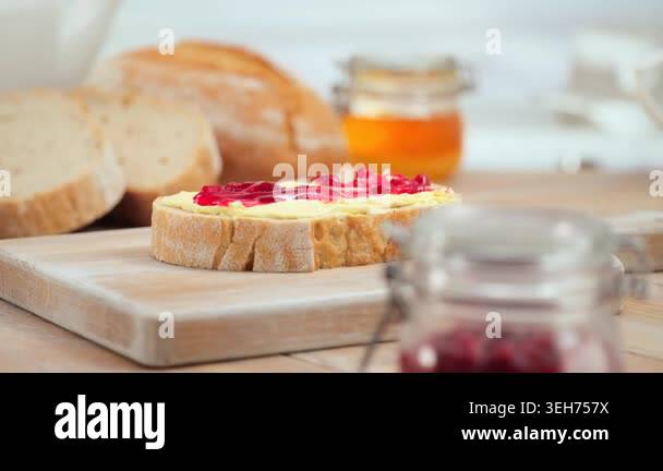 Sweet berry jam being spreading on fresh bread slice, rustic kitchen ...