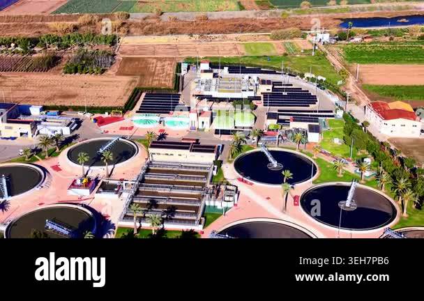 Aerial view of industrial clarifier tanks and rows of photovoltaic ...