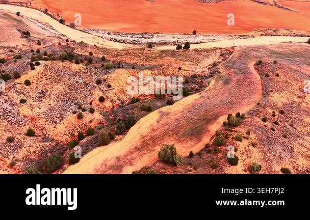 Winding dirt track and dry riverbed through red soil landscape with ...