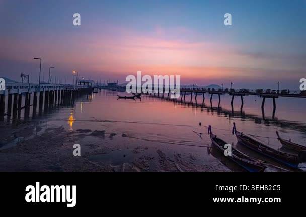 Calm water reflects a vibrant sunset over a wooden pier in a tranquil ...