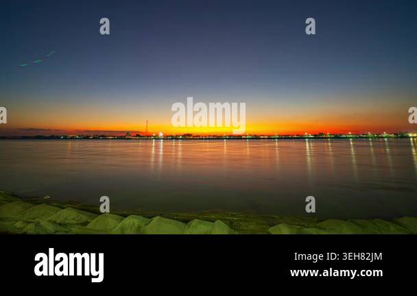 Vibrant sunset over calm water reflecting city lights in a serene ...