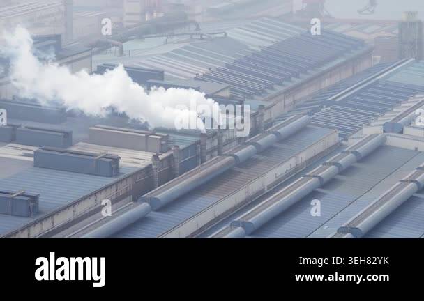 Aerial view of a large industrial complex with white smoke billowing ...