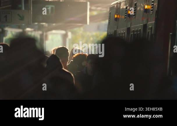 People walk through a train station as sunlight filters in, creating ...