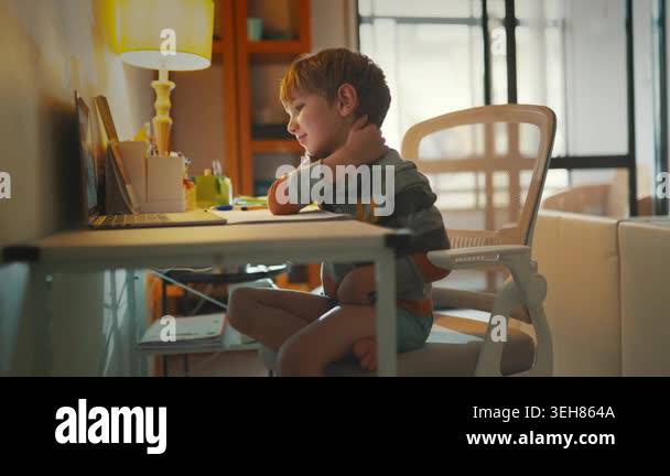 Young child sits cross-legged at a desk and smiles while looking at a ...