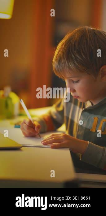 A child is focused on drawing at a desk in a cozy room. The warm light ...