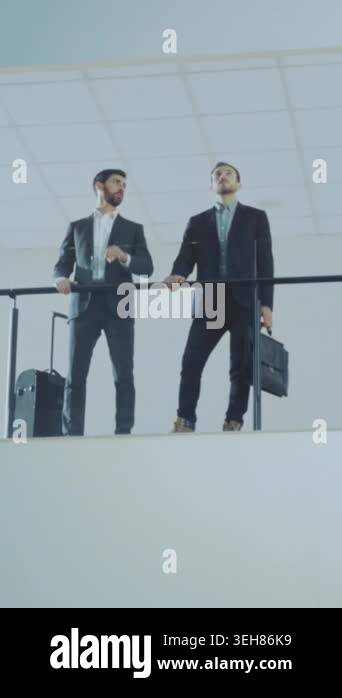 two colleagues shake hands on balcony above terminal, suitcases and ...