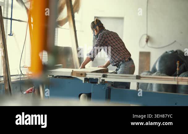 Skilled craftsman wearing a respirator mask processing a wooden plank ...