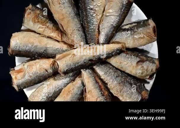 A seamless 4K video loop of small, whole fried fish rotating slowly on ...