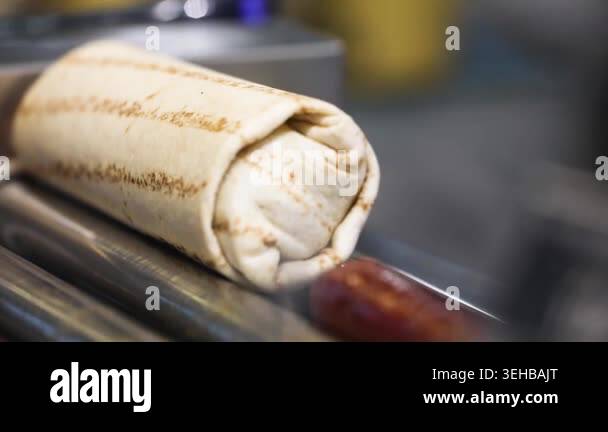 Close-up of a hot dog wrapped in lavash being cooked on a grill at a ...
