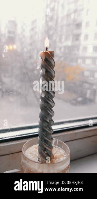 Burning spiral candle sits in a glass holder on a windowsill ...