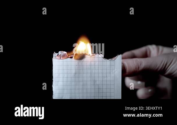 A hand holds a piece of grid paper and ignites the edge with a lit ...