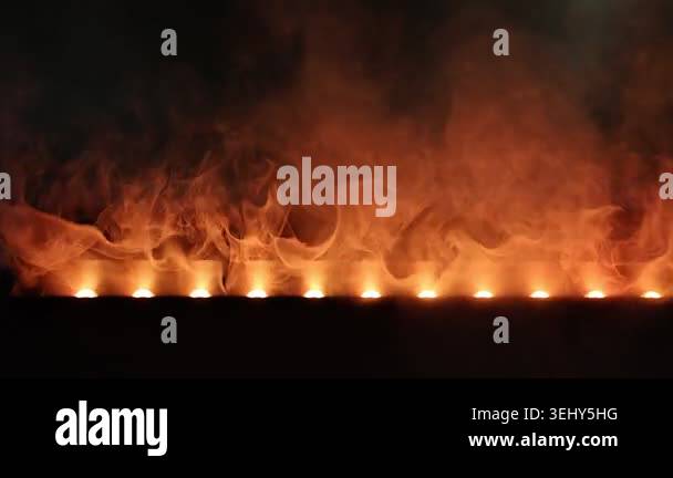Row orange flames and smoke over dark stage, glowing embers on gas ...
