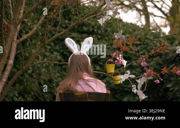 Woman wearing Easter bunny ears sits by easter decorations on blossom ...