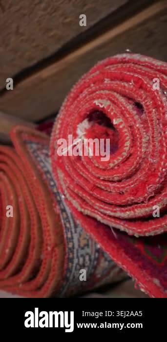 Stacked rolls of traditional red woven carpets rest tightly on rustic ...