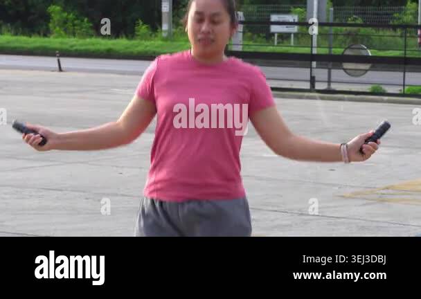Young Asian woman in pink t-shirt skipping rope and jumping outdoors ...