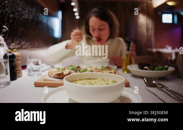 Woman eating soup at a restaurant table with a bowl of creamy soup in ...