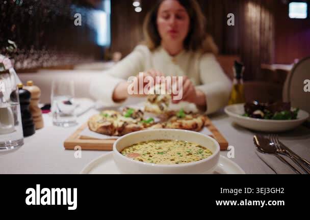 Woman eating soup at a restaurant table with a bowl of creamy soup in ...