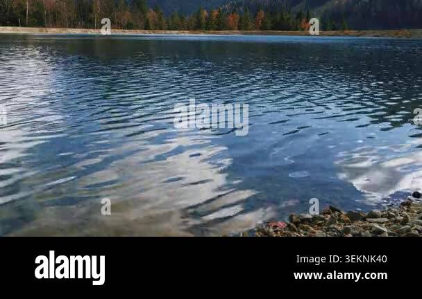Water ripples move across a lake surface with reflected clouds and a ...
