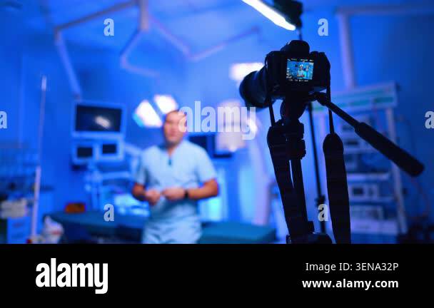 Camera filming doctor standing in blue surgical operating room. Tripod ...