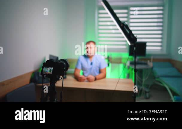 Studio camera filming man at desk under green ambient lighting ...