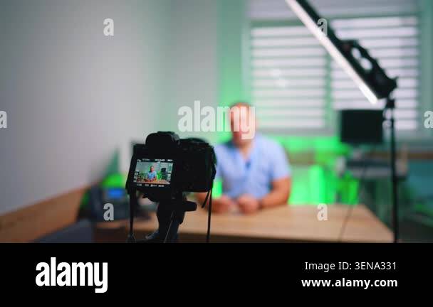 Mirrorless camera filming presenter seated at desk with green light ...