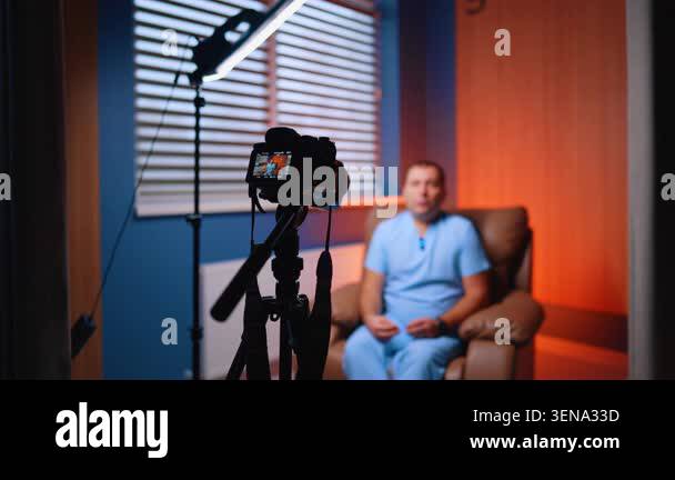 Camera filming seated man in armchair with orange wall accent ...