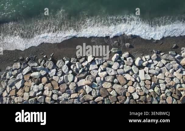 Aerial top-down view of turquoise sea waves breaking on a pebble beach ...