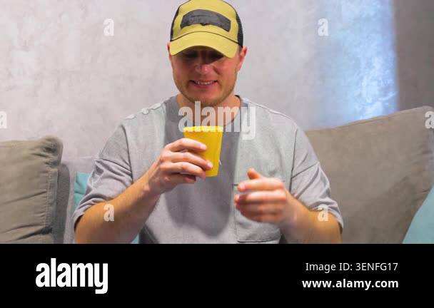 A man drinks tea from a yellow plastic cup at home. A young guy drinks ...