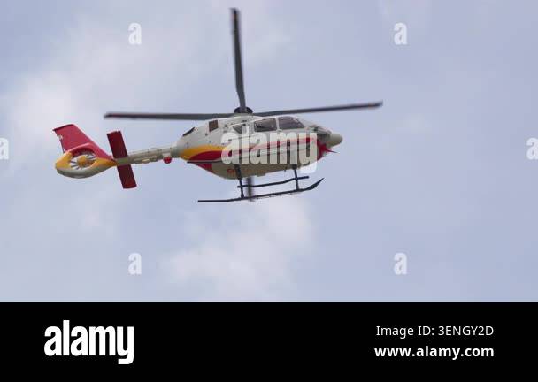 A red white and yellow helicopter with twin landing skids flies in ...