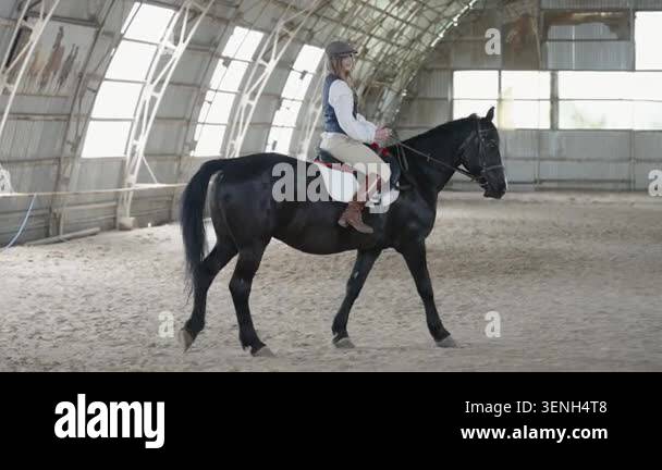 Young female jockey riding black horse in an indoor arena Stock Video ...