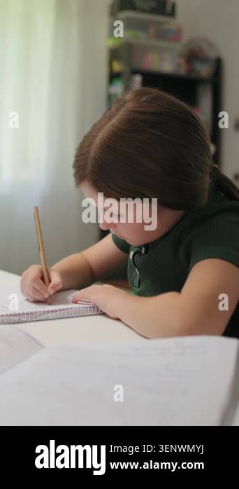 A focused young girl sits at a desk at home, diligently writing her ...