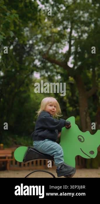 Blonde caucasian toddler confidently riding green playground rocker ...