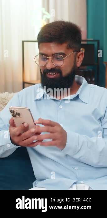 Indian man at home scrolls smartphone news feed smiles as liked post ...