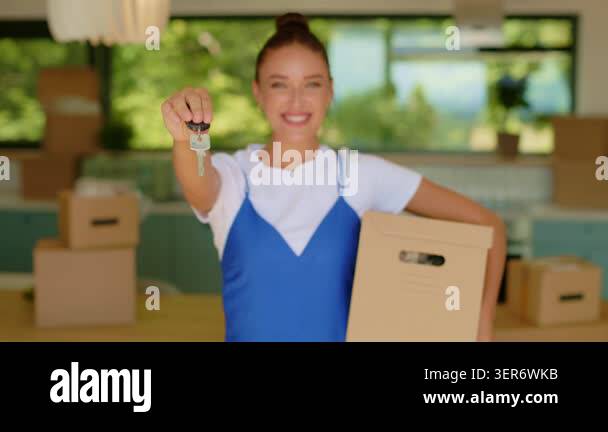 Happy woman presenting house keys toward camera and holding cardboard ...