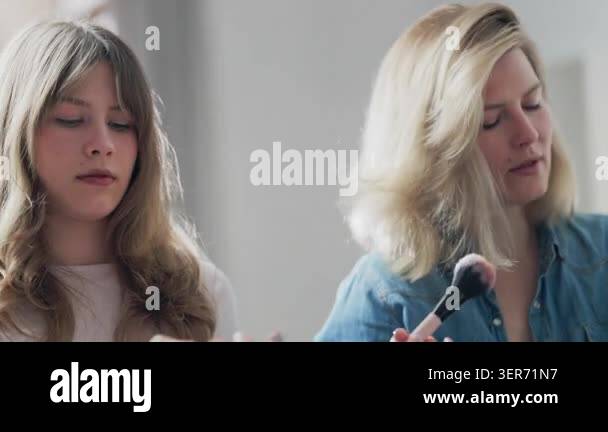 Young blonde daughter learning makeup application from her mother while ...