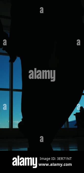 A person sits quietly in an airport while looking out the large window ...